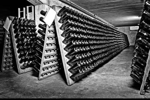 A black and white picture of a wine storage system in the Lini 910 Winery. The scene features rows of wine bottles neatly stacked at a slanted angle in wooden slots.