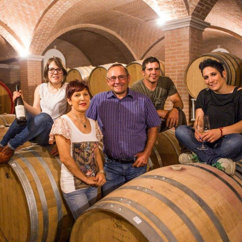 A picture of the Monte Tondo family inside the winery building surrounded by large barrels. A woman on the left can be seen holding a wine bottle.